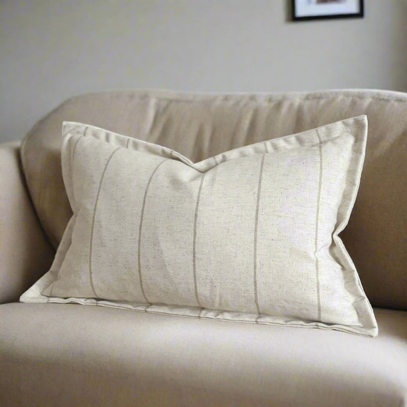 A rectangle cushion with a flanged edge. Cream, stone colour with a subtle vertical beige stripe repeating from left to right. Sat on a cream sofa
