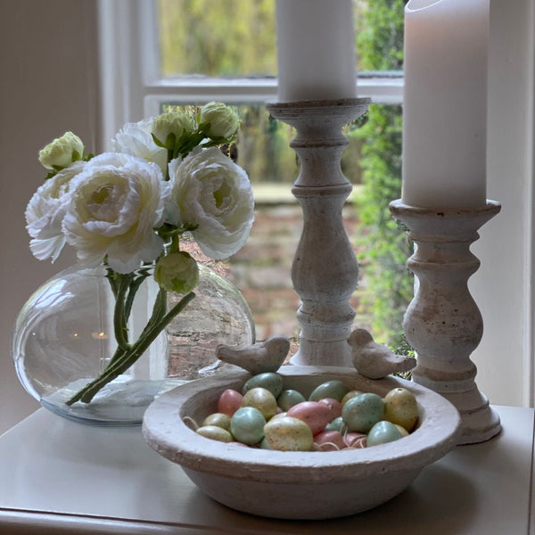 Stone bird bath with 2 stone birds sat around the edge of the bowl. Sat on a sideboard filled with decorative pastel easter eggs for decoration