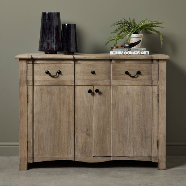 Front view of a brown wood sideboard with a bleached effect. 1 drawer along the top with 2 black iron handles and 2 doors at the bottom. Styles with books and vases on top.